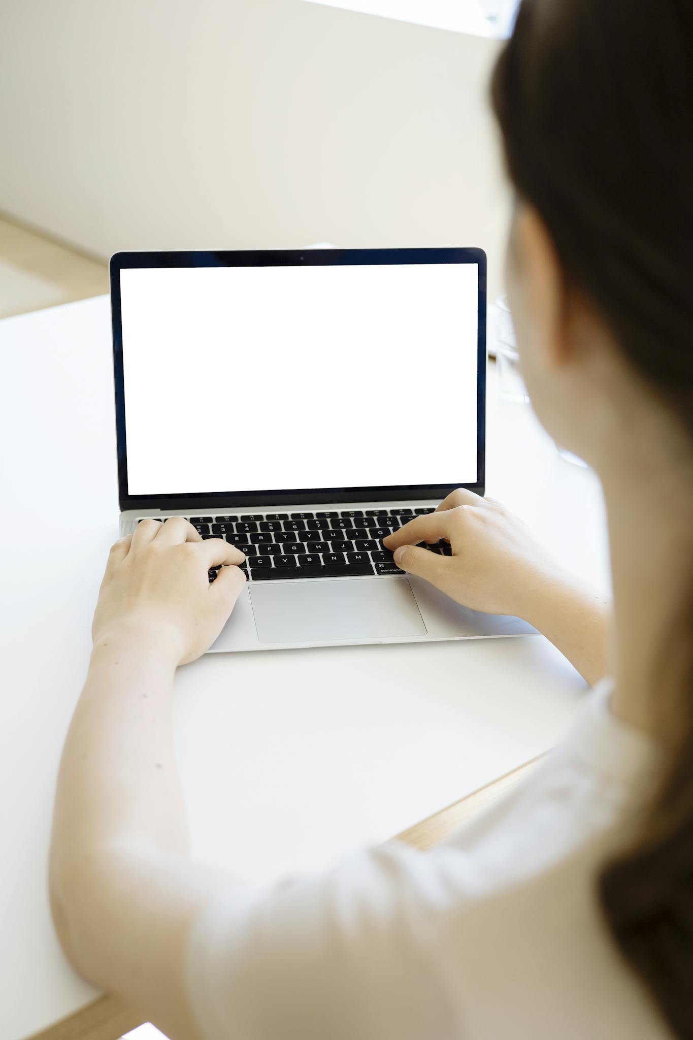 A woman typing on a laptop with a blank screen, ideal for mockups.