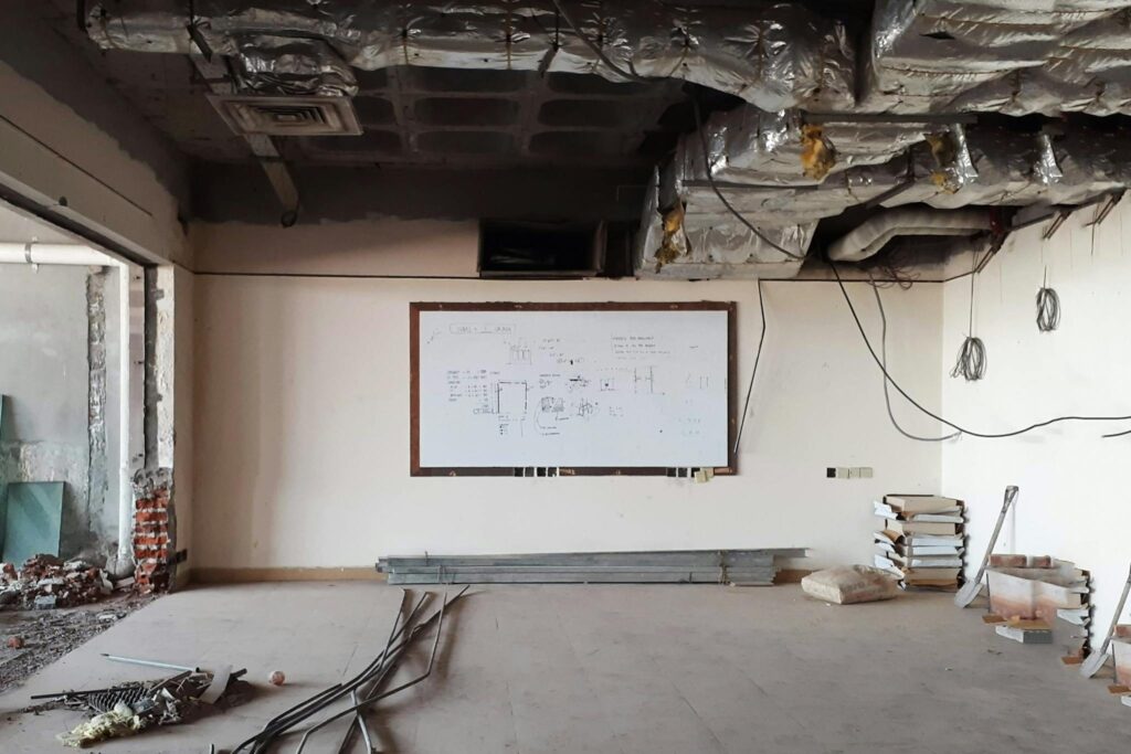 An empty room under construction with exposed ceiling ducts and a whiteboard.