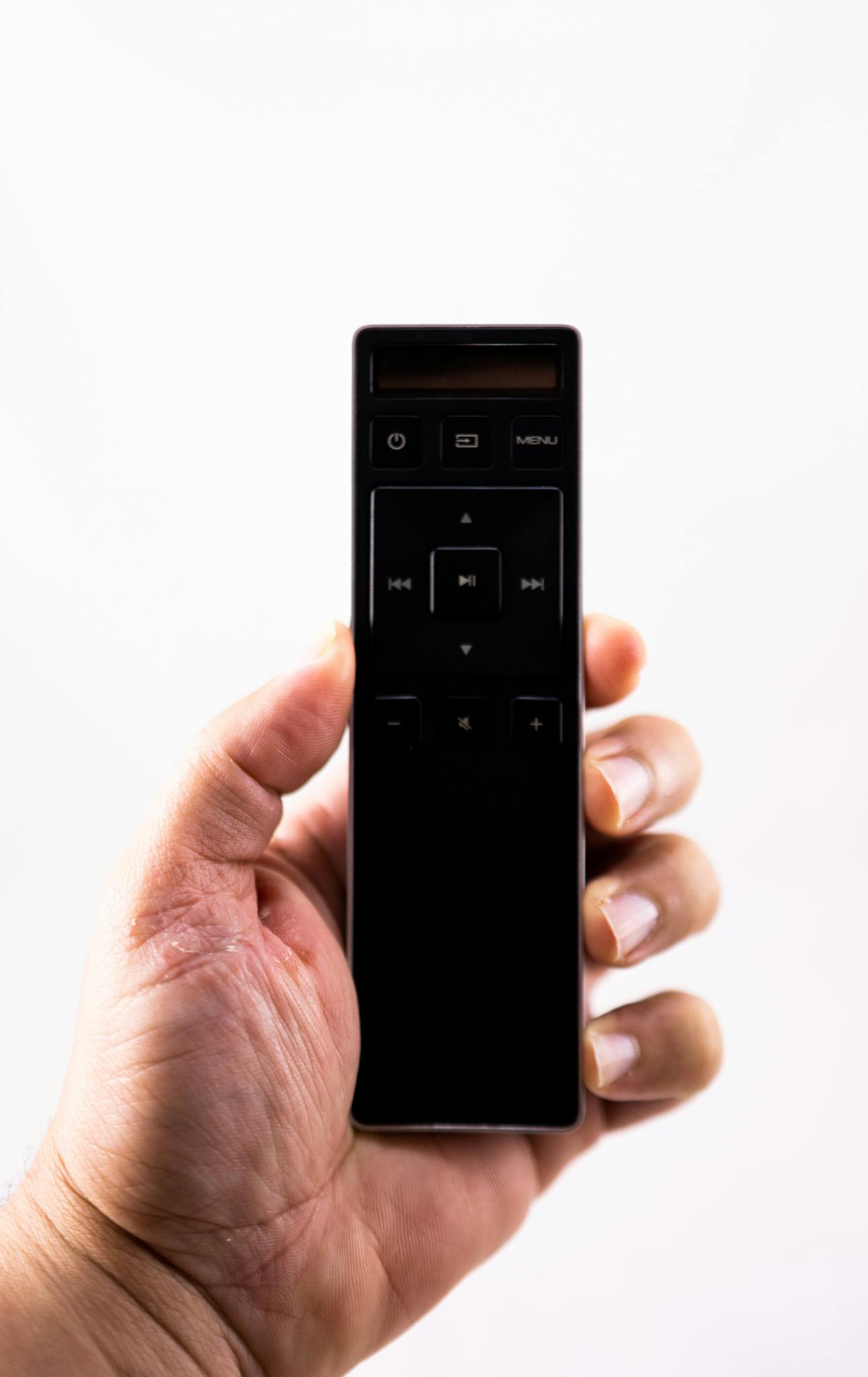 Crop unrecognizable person showing remote control with buttons on white background in studio